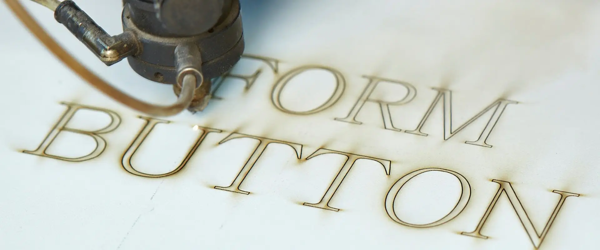 A laser engraving the words FORM BUTTON into a light surface