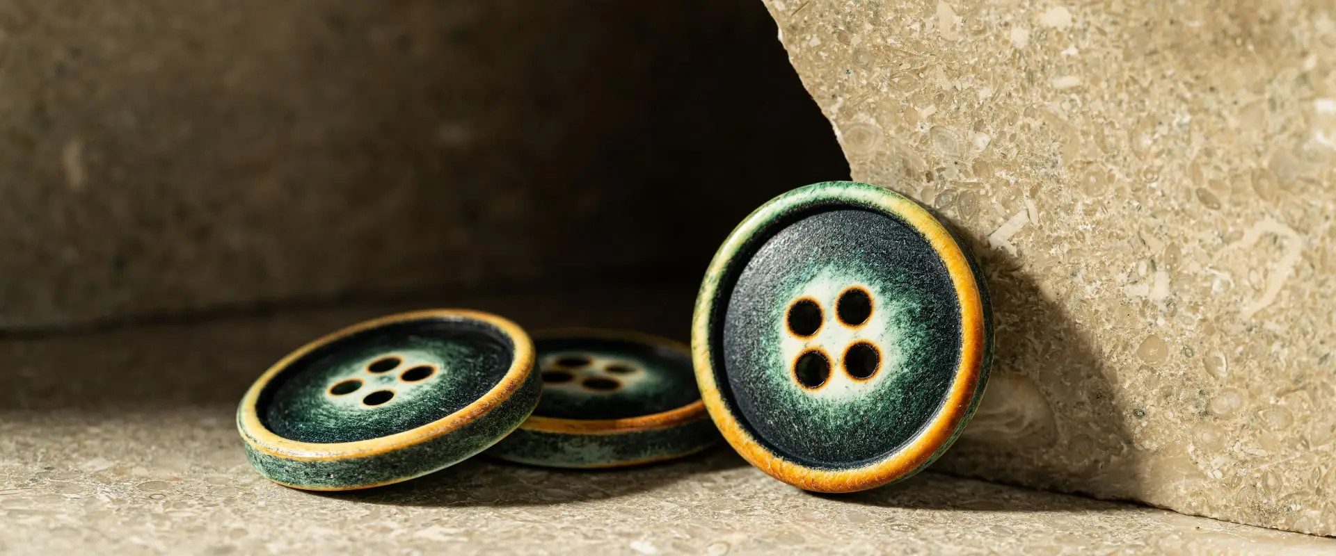 Two green-and-ochre natural buttons against stone