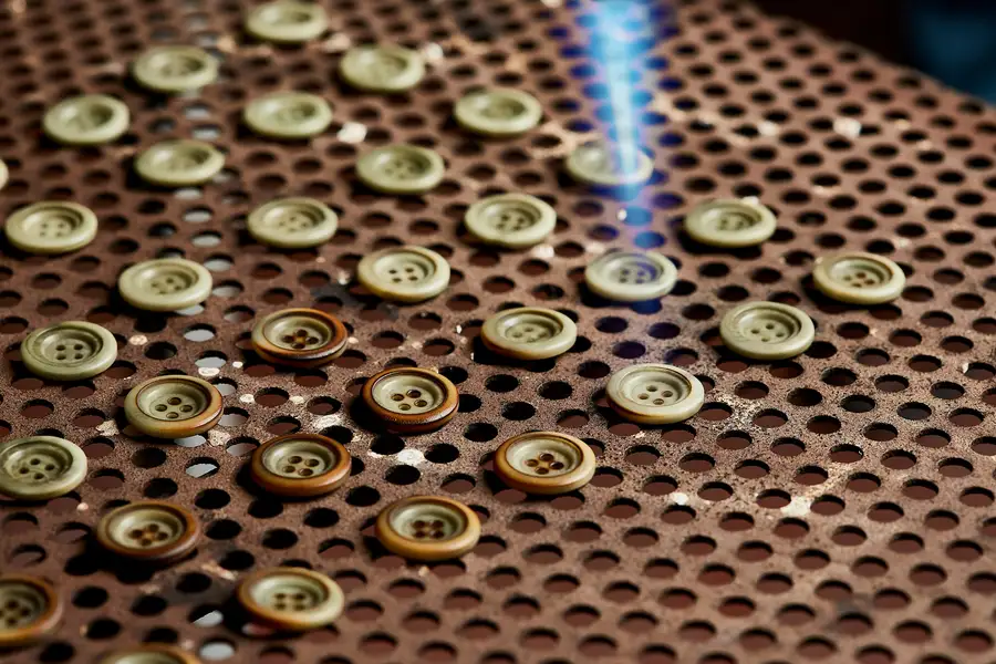 Buttons on a perforated tray under a blue laser beam