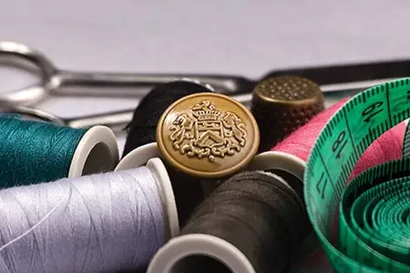 A crested metal button among spools of thread and a tape measure